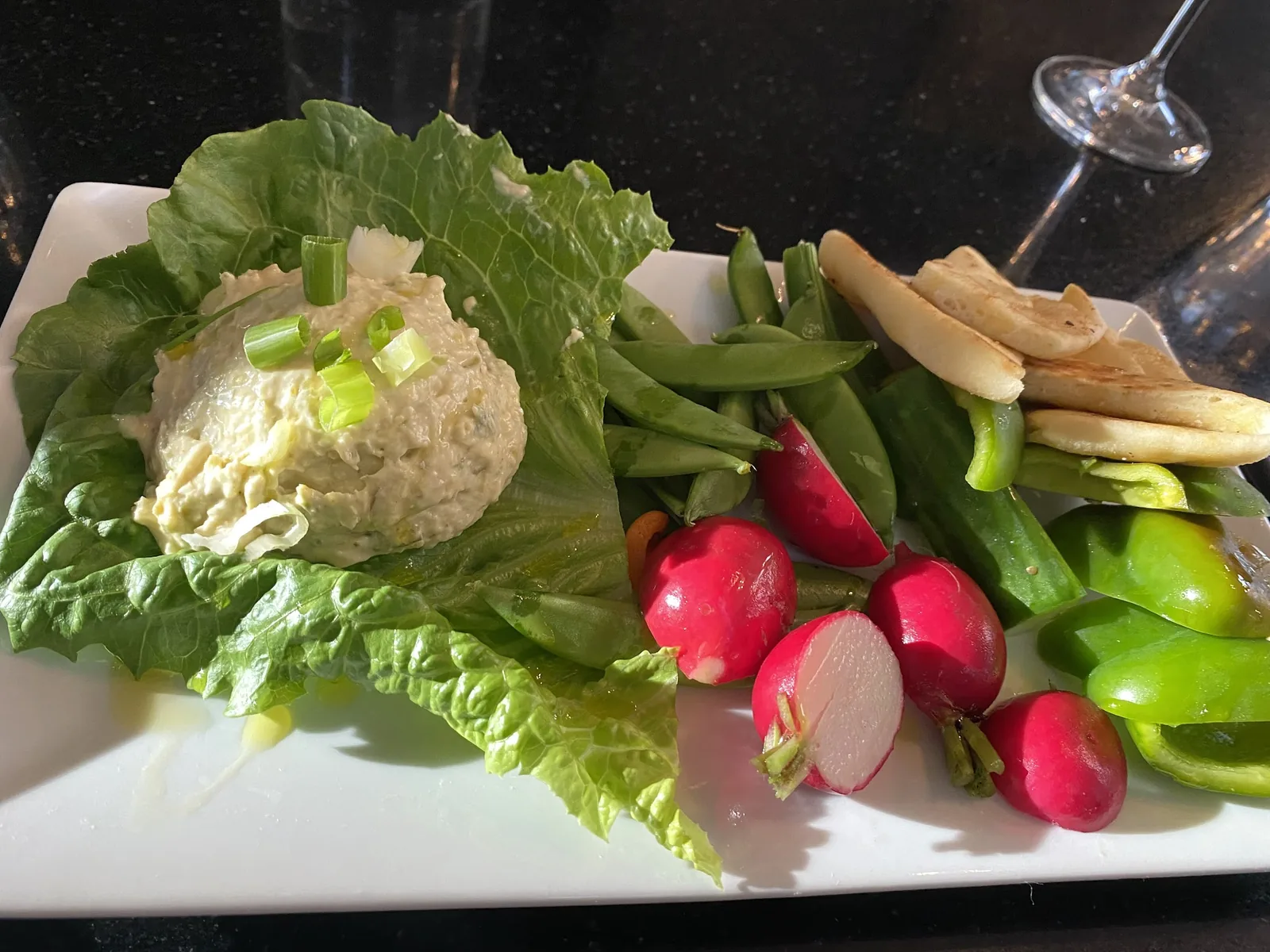 A plate of curry chicken salad on greens with radishes and grilled bread