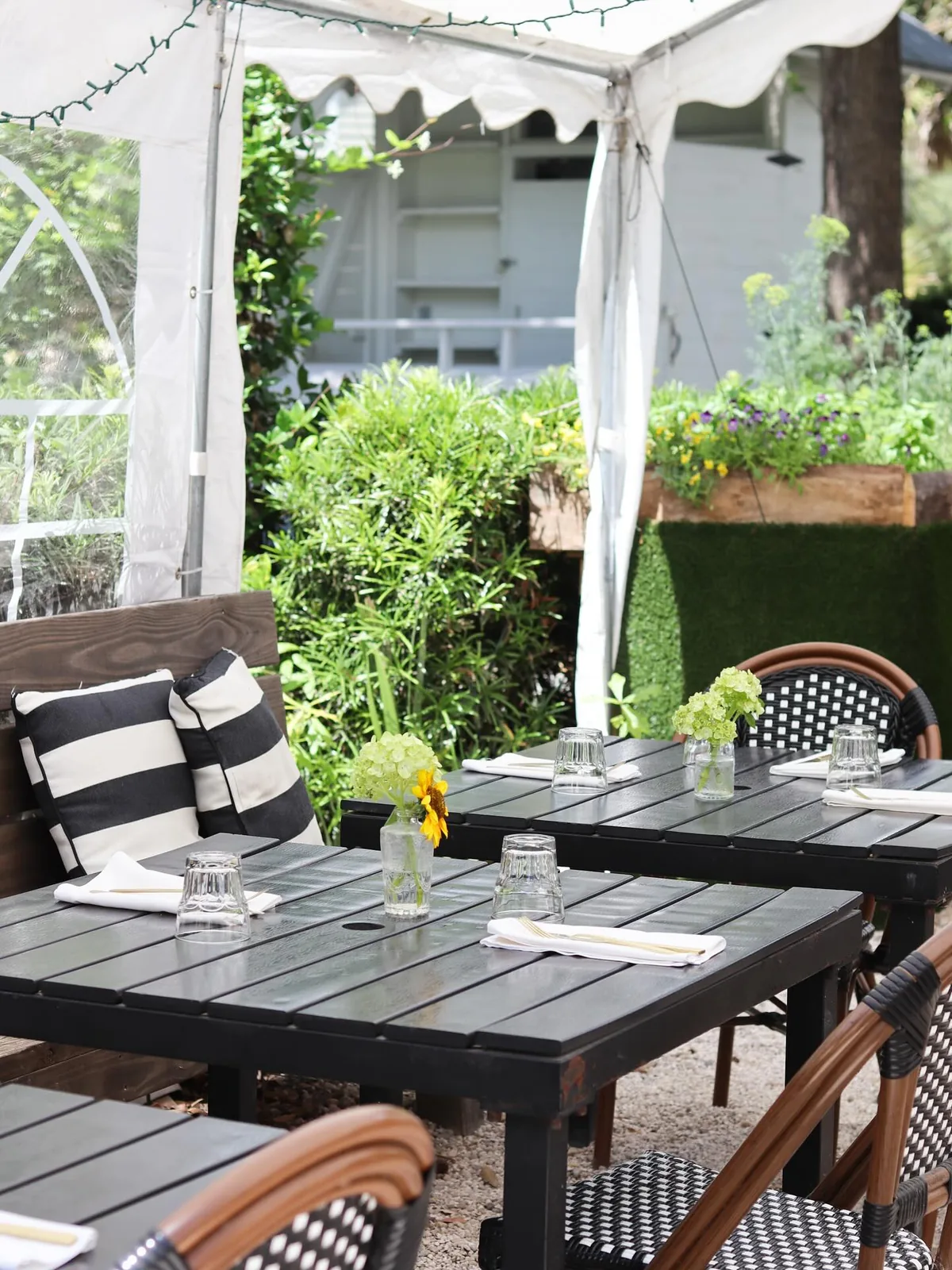 A patio table set beside a raised planter box of flowers and herbs, with a sunflower in a jar